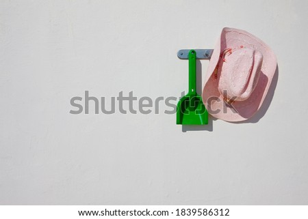 Cowboy hat and plastic shovel hanging on a wall hook in bright daylight.