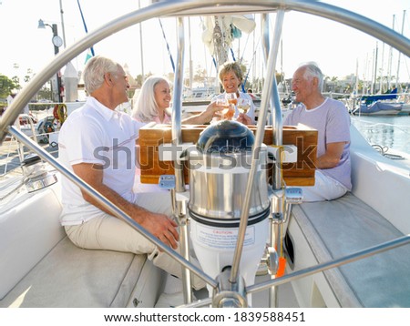 Portrait of a senior couple with friends seated in a sailing boat clinking wine glasses as seen through the steering wheel.