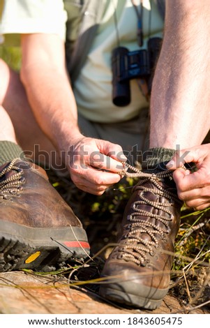 The front view of the hiker man ties the laces on his shoe during a holiday backpacking in the forest.