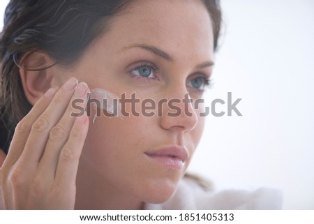 Horizontal head and shoulder profile shot of a young woman applying cream to face.