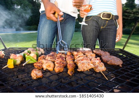 Horizontal mid section of a couple having barbeque outdoors stand by the grill with wine glasses in hand.