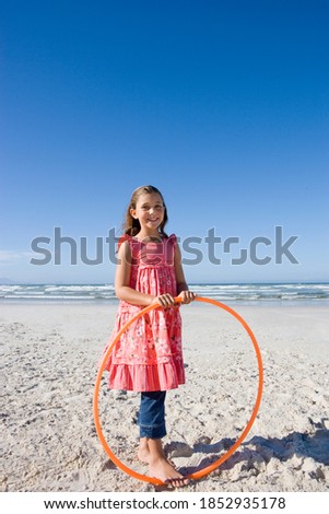 Vertical portrait of a girl with a plastic hoop on the beach smiles at the camera.