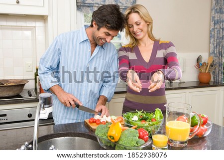 Horizontal waist up shot of a happy husband and wife making fruit salad in the kitchen.