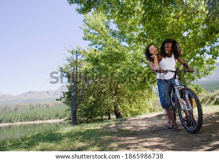 Horizontal low angle shot of a joyous couple sitting in tandem on a mountain bike by the lakeside on a woodland trail with copy space.