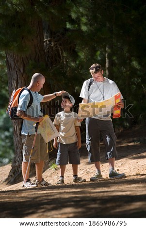 Vertical shot of a boy hiking on a woodland trail with his father and grandfather with father consulting a map.