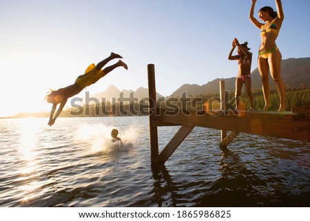 Profile shot of a father and son jumping off a jetty into the lake at sunset with a splash as the daughter and mother cheers on.