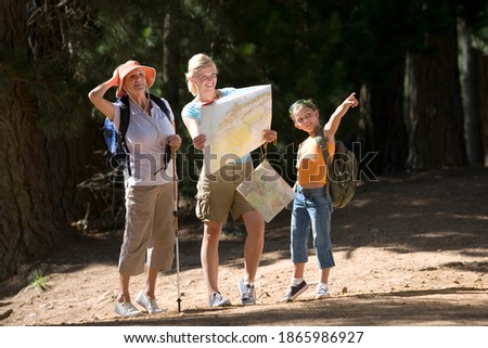 Girl hiking on a woodland trail with her mother and grandmother points to something as her mother consults a map.