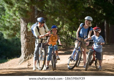 Horizontal shot of a family of four mountain biking along a woodland trail with father adjusting strap of daughter\'s cycling helmet.