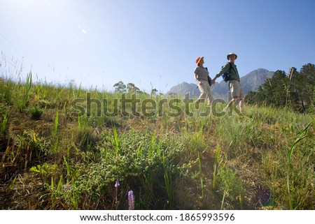 Horizontal low angle shot of a senior couple walking holding hands during hiking on a mountain trail on a sunny day.