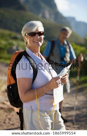 Selective focus on a woman holding a map hiking on a mountain trail with her husband in the background.