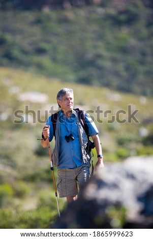 Vertical shot of a mature man hiking on a mountain trail with a hiking pole with copy space.