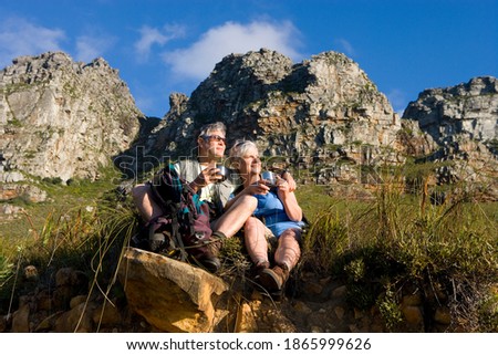 Horizontal low angle shot of a seated mature couple hiking on a mountain trail taking a coffee break admiring the scenery around.