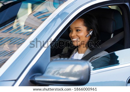 Horizontal portrait of a smiling businesswoman wearing a mobile hands free drives a car.