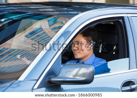 Horizontal portrait of a smiling businessman wearing a mobile hands free drives a car.