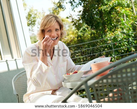 Horizontal three quarter length shot of a woman having strawberries in breakfast smiles at the camera.