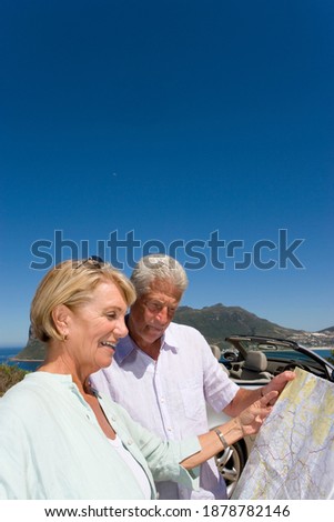 Vertical shot of an old couple looking at a map on the coastal highway on a bright sunny day.