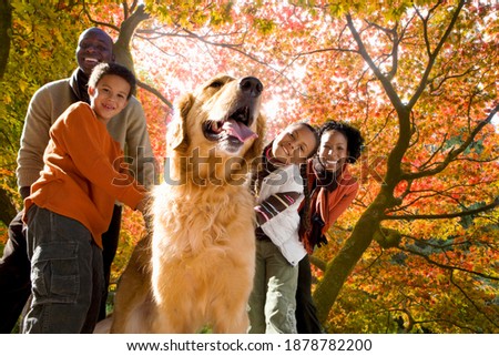 African family of four looking happily at the camera while walking their dog in the park on a sunny autumn day.