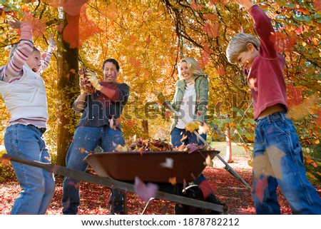 A family of four enjoying doing yard work in autumn as the kids are playing with autumn leaves.