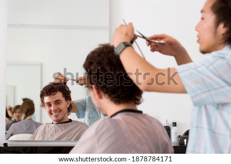Head and shoulder close-up of a barber cutting client\'s hair with reflection in the mirror and focus on the same.