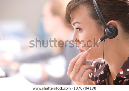 Horizontal head and shoulder profile shot of a stressed young woman adjusting her headset at desk in office with copy space.