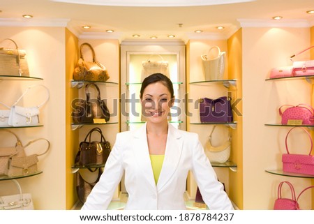 Saleswoman working in a bag showroom with the shelf full of bags in the background.
