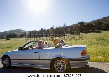 Wide profile shot of a joyous senior couple with friends in an convertible car outdoors on a road trip.