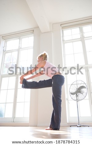 Full length low angle portrait of a young woman with hands holding a stretched leg towards a side indoors.