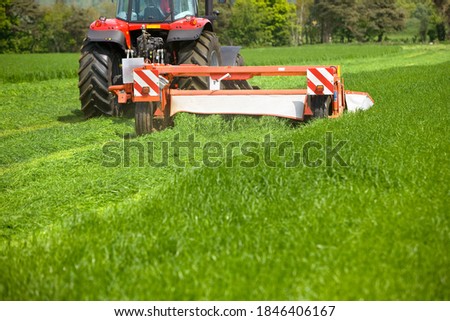 A medium closeup of a flail mower attached to a tractor running through the field while cutting the grass for silage