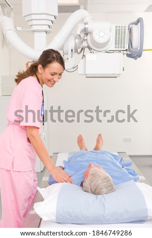 A side view of a young adult radiologist in pink scrub suit helping her patient with the x ray machine