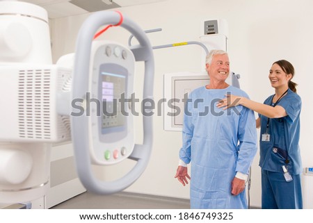 A qualified and helpful radiologist in selective focus assisting her patient with the X-ray machine placed in the foreground of a clinic