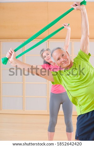 A vertical front view of senior-adult man and woman smiling at the camera while exercising in a gym using resistance bands