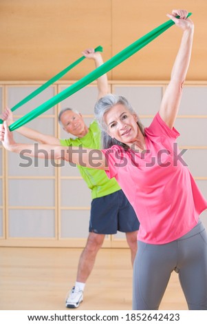 A senior-adult man and woman working out in a gym using resistance band in selective focus