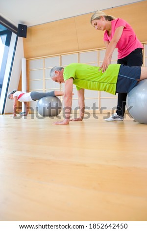 A low angle view of an activity room in a gym with a personal trainer helping senior adults balance on a fitness ball in the exercise class
