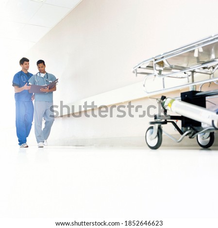 A full-length wide shot of a hospital corridor with Doctors in scrubs discussing a medical chart
