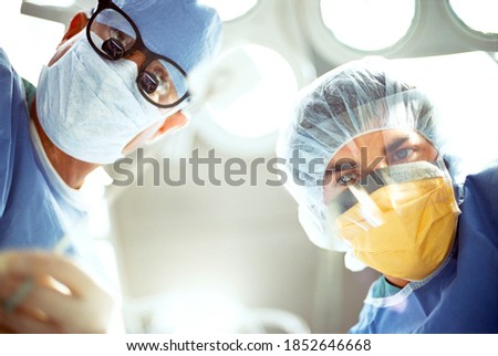 A low angle POV of a patient seeing two surgeons in surgical masks under surgery lamp while looking down at him