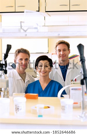 A portrait of smiling pharmacists wearing scrub suits and lab coats in the hospital pharmacy with selective focus