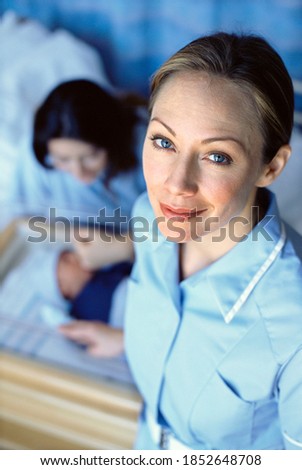 A high angle Portrait of a smiling nurse with newborn baby boy and his mother in the background