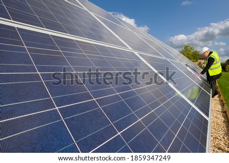 A medium shot of a worker with safety jacket checking a large solar panels in a field.