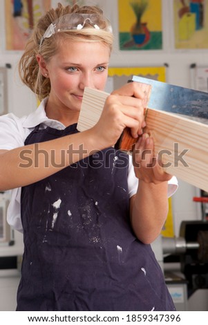 A portrait shot of a young blonde girl measuring planed wood in a vocational school.