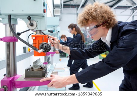 A side profile close up shot of a young boy using a drill machine in a vocational school.