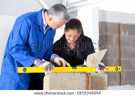 A shot of a teacher teaching a young girl how to use level tool in a bricklaying vocational school.