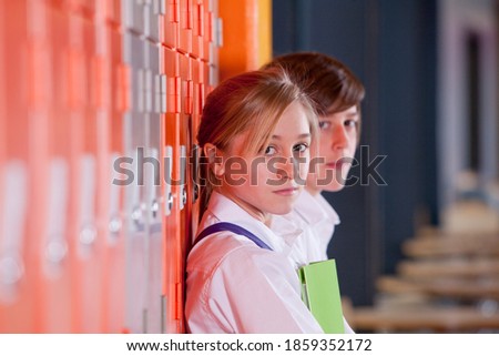A close up shot of two young students leaning against school lockers and looking at camera.