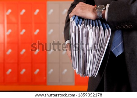 A close up shot of teacher\'s hands holding files with lockers in background.