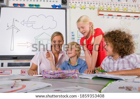 A low angle medium shot of a happy teacher holding a model wind turbine while her curious students examines it in a classroom.