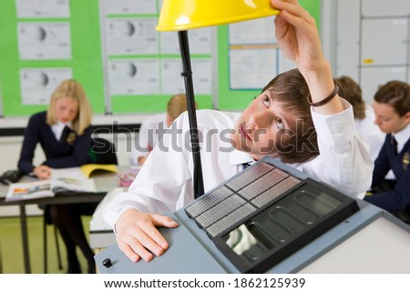 A close up shot of a young boy adjusting lamp on a model house with solar panel in a science class.
