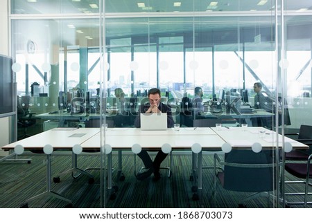 A full-length view of a serious businessman in a formal suit sitting at the laptop in the conference room