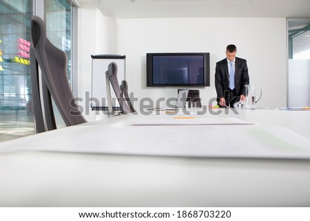 A wide view of a businessman standing in a meeting room while reviewing paperwork at the table