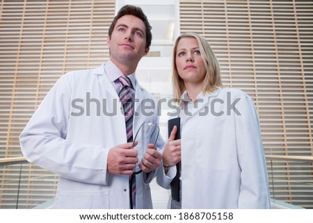 A low angle view of two serious doctors wearing lab coats as they stand in the hospital corridor while holding a stethoscope and a report