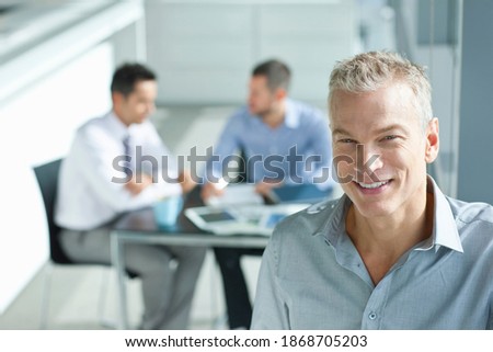A high angle portrait of a smiling businessman with co-workers having a meeting in the background