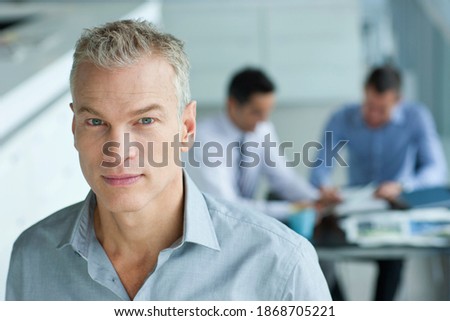 A high angle portrait of a serious businessman with co-workers having a meeting in the background